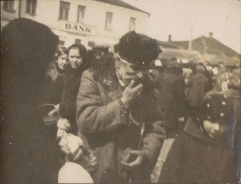 Sialianie na rynku na fonie kamianicy z šyĺdaj Dzisienskaha kaapieratyŭnaha banka ŭ Hlybokim